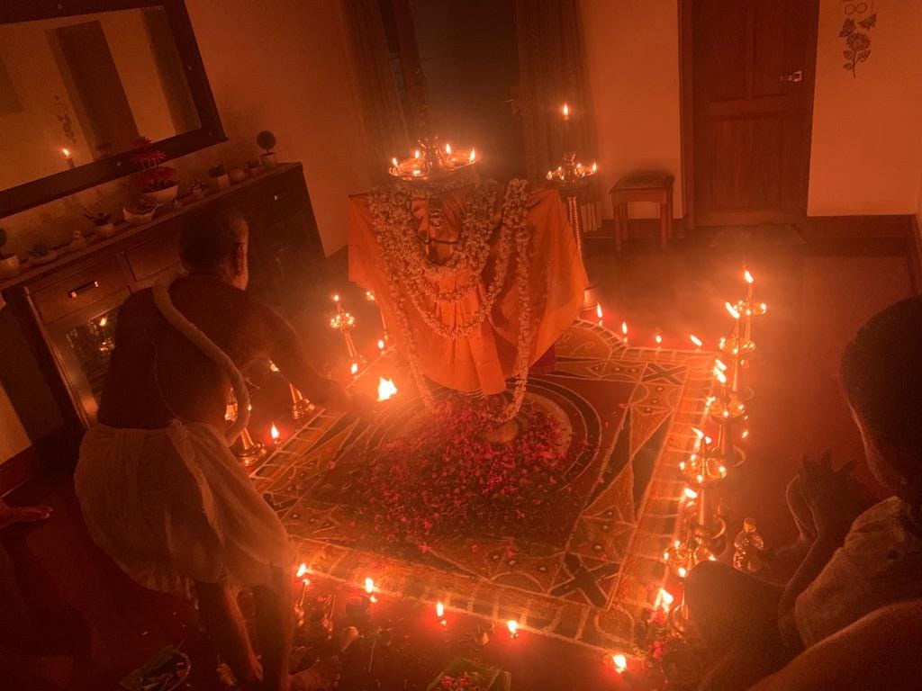 Guruji performing an evening pooja with oil lamps and floral offerings